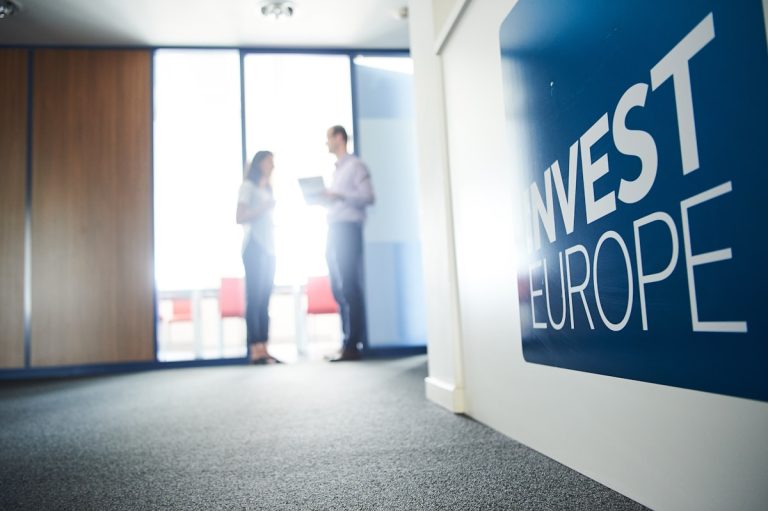 Two blurred people converse in an office next to an
