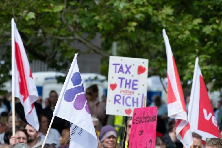 People protesting with flags and a "tax the rich" sign