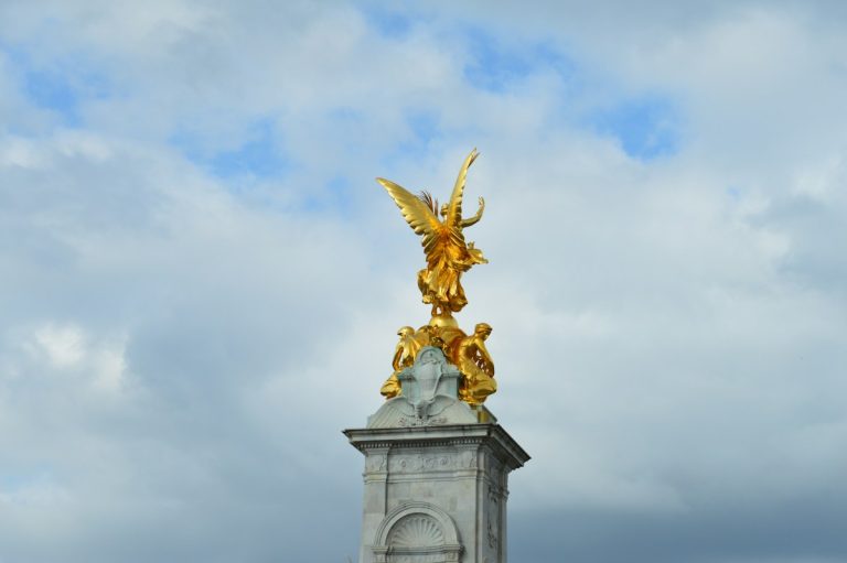 Golden statue atop a stone monument against cloudy sky