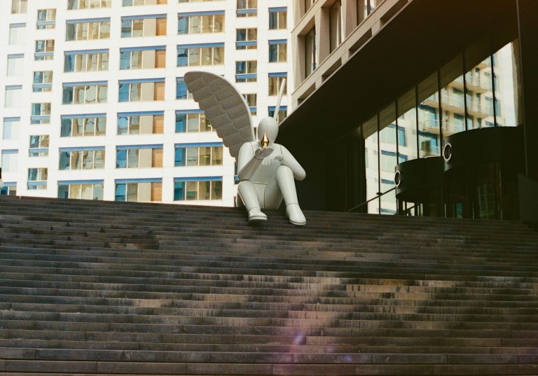 White angel statue sitting on stairs outside a modern building