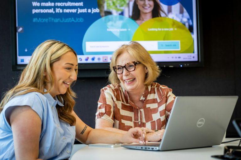 Two women looking at a laptop screen in a modern office workspace